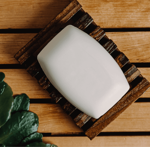 White soap bar on a wooden soap dish with a plant in the corner